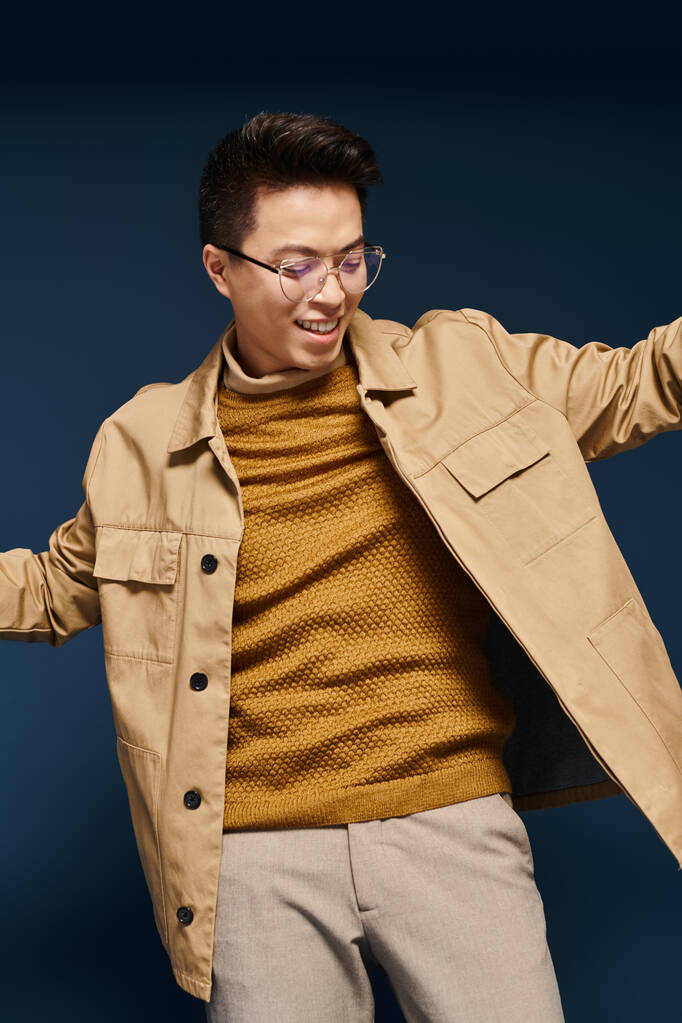 Um jovem na moda em óculos e uma jaqueta bronzeada faz uma pose, exalando confiança e sofisticação. - Foto, Imagem