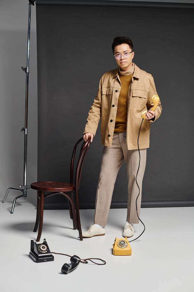 Un jeune homme à la mode se tient avec confiance à côté d'une chaise, tenant le téléphone - Photo, image