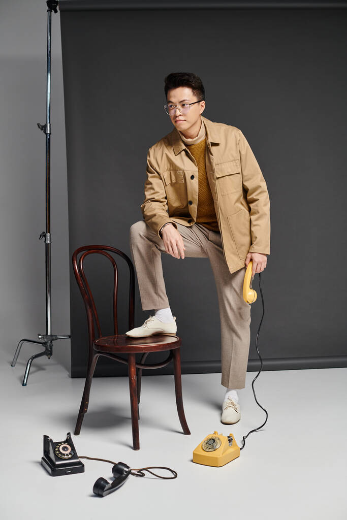 Модний молодий чоловік в елегантному вбранні сидить на стільці поруч з телефоном, виключаючи впевненість і харизму. - Фото, зображення