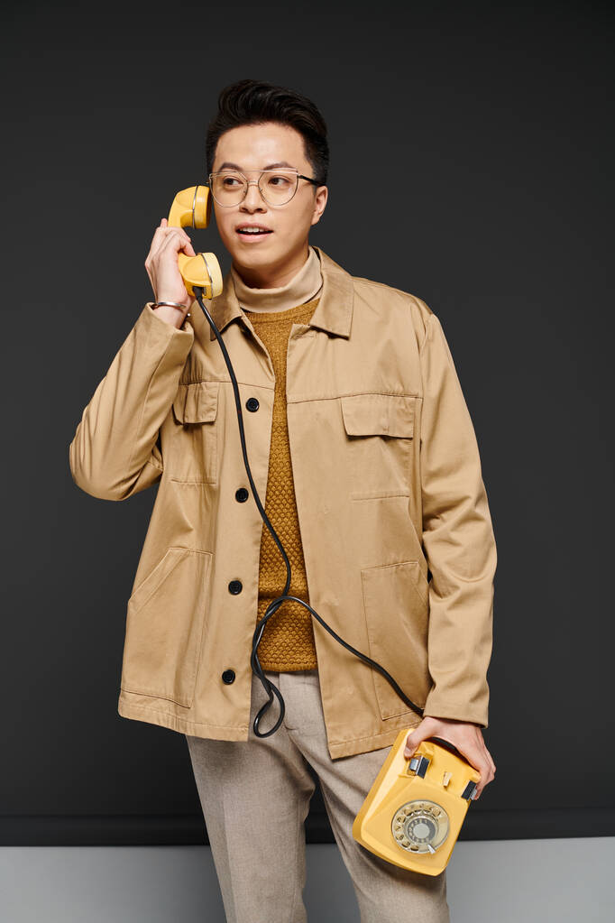 Модный молодой человек в коричневой куртке активно взаимодействует с желтым телефоном. - Фото, изображение