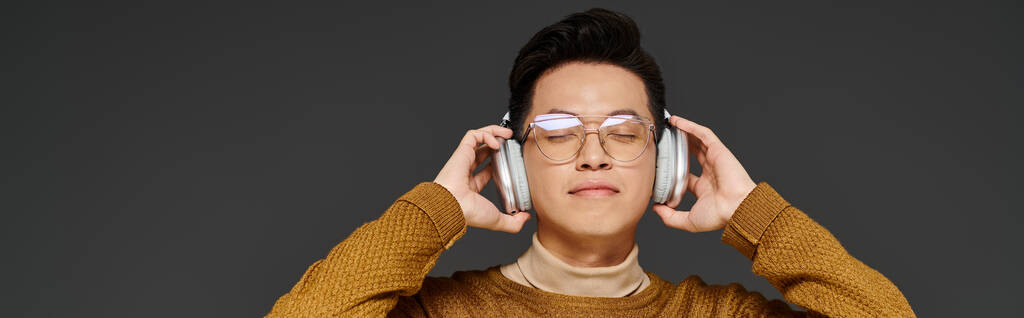 Un jeune homme à la mode portant des lunettes et des écouteurs, activement engagé dans la pose. - Photo, image