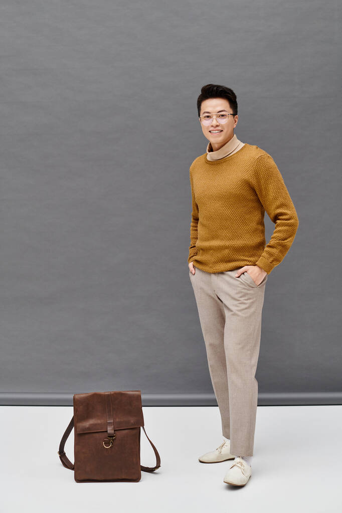 Un joven de moda con un atuendo elegante se encuentra junto a una bolsa marrón, exudando estilo y misterio. - Foto, imagen