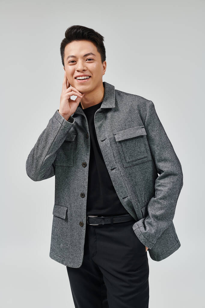 Egy divatos fiatalember dinamikus pózt üt egy elegáns szürke dzsekiben és fekete ingben, kifinomultságot és magabiztosságot sugározva.. - Fotó, kép