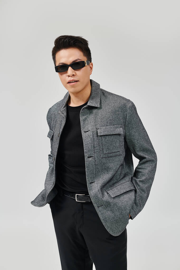 Un joven de moda emana confianza en una chaqueta gris y pantalones negros, posando creativamente con energía vibrante. - Foto, imagen