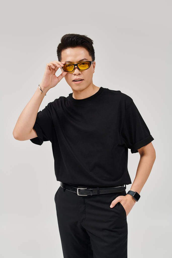 Un jeune homme à la mode dans une chemise noire frappe une pose, exsudant la confiance avec ses lunettes de soleil. - Photo, image