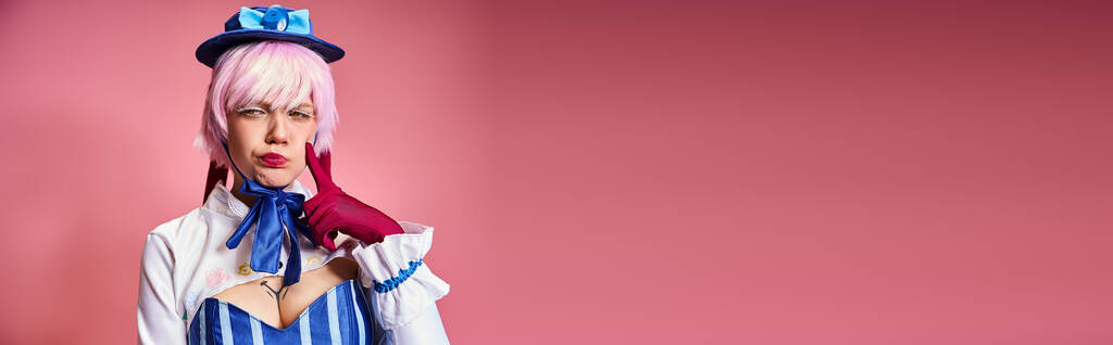 ελκυστική γυναίκα cosplayer με κόκκινα γάντια και μπλε καπέλο θέτει συναισθηματικά σε ροζ φόντο, πανό - Φωτογραφία, εικόνα