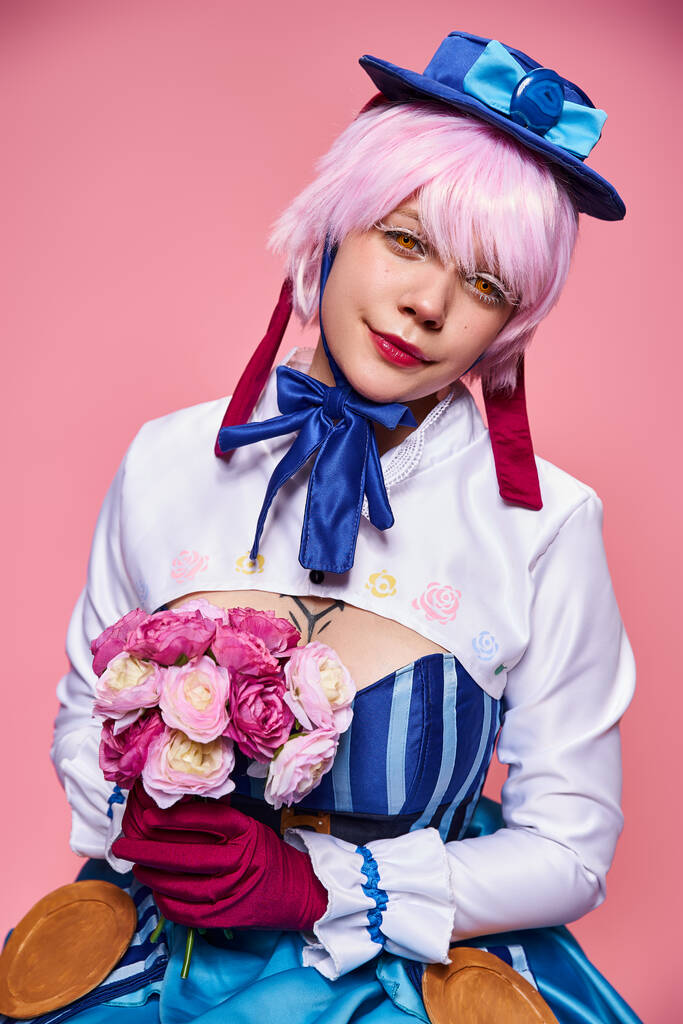 cute jolly female cosplayer in bright anime costume holding pink flowers and looking at camera - Photo, Image