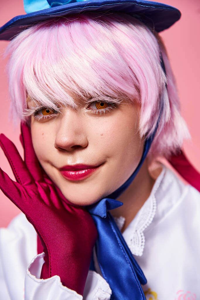 glamorous sexy female cosplayer in blue hat and vibrant attire looking at camera on pink backdrop - Photo, Image
