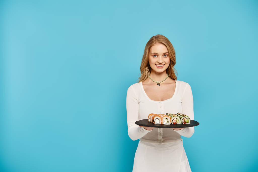 Une belle femme blonde tient délicatement une assiette de rouleaux de sushi colorés, mettant en valeur la délicieuse cuisine asiatique. - Photo, image