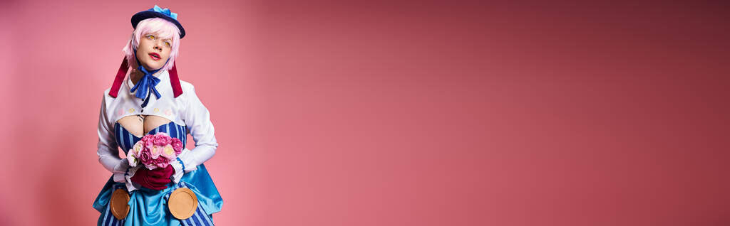 modish cosplayer v pulzující oblečení drží růžové květy a odvrací pohled na růžové pozadí, prapor - Fotografie, Obrázek