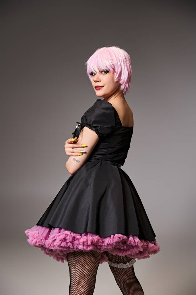 сексуальна стильна жінка в чорній сукні з рожевим волоссям, що займається аніме персонажем і дивиться на камеру - Фото, зображення