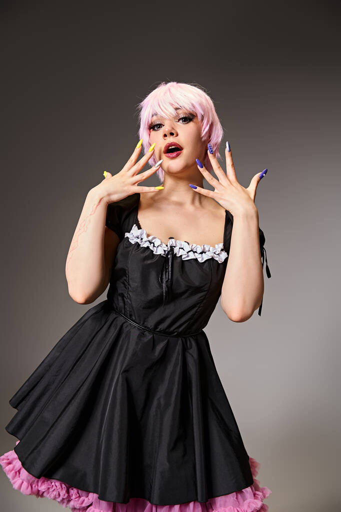 atrakcyjna elegancka kobieta w czarnej sukience z różowymi włosami cosplaying anime postać i patrząc na aparat - Zdjęcie, obraz