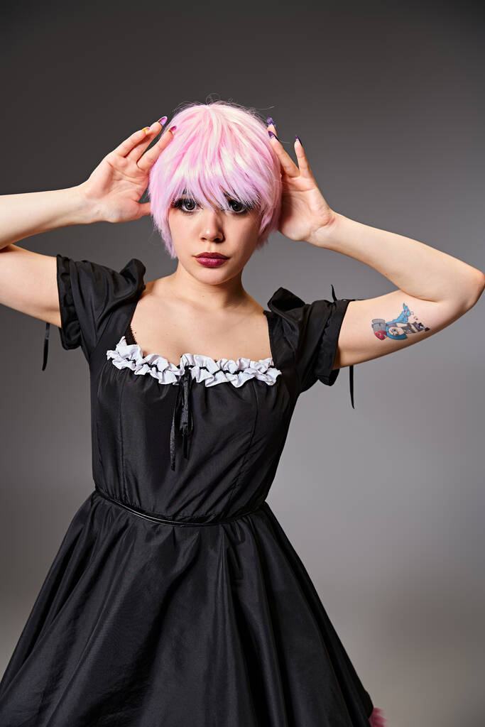 atractiva mujer elegante en vestido negro con el pelo rosa personaje de anime cosplaying y mirando a la cámara - Foto, imagen