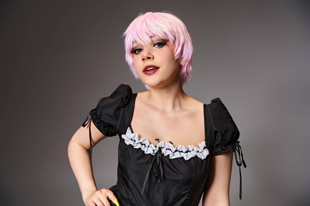 grazioso cosplayer seducente in costume da cameriera sexy con i capelli rosa guardando la fotocamera su sfondo grigio - Foto, immagini