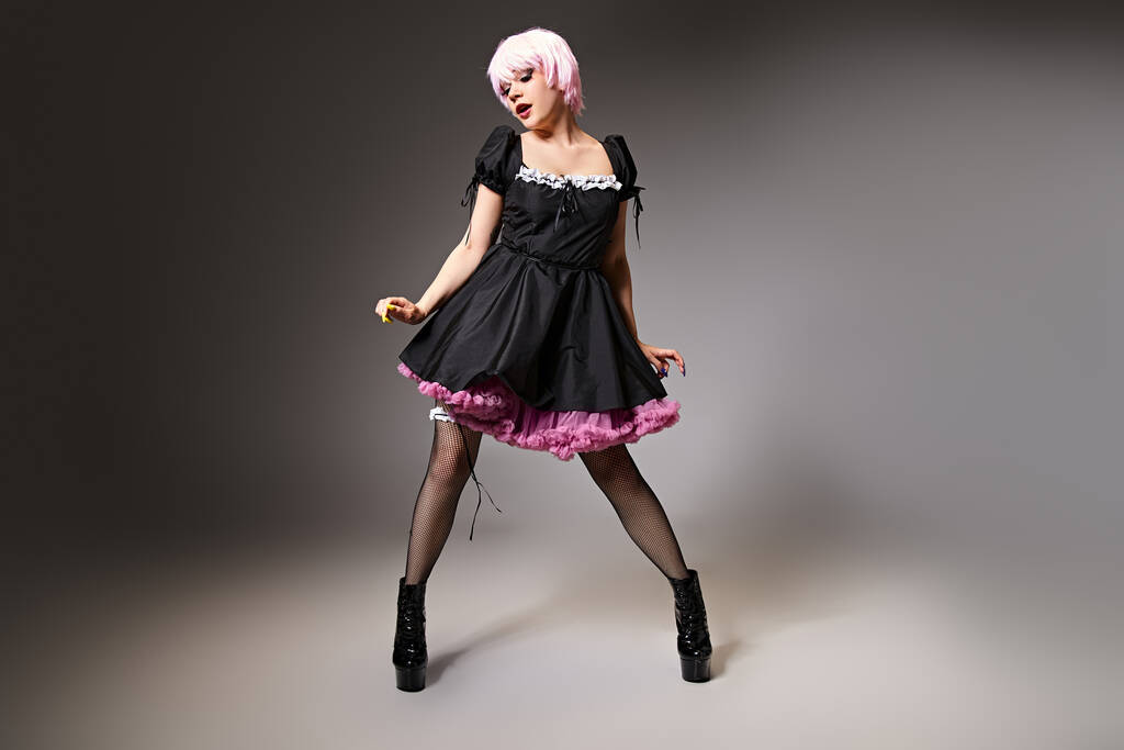 piękne różowe włosy cosplayer w sexy pokojówka kostium pozowanie na szary tle i patrząc daleko - Zdjęcie, obraz