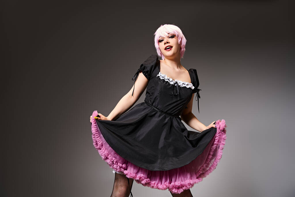 vrij aantrekkelijk cosplayer in sexy meid kostuum met roze haar op zoek naar camera op grijze achtergrond - Foto, afbeelding