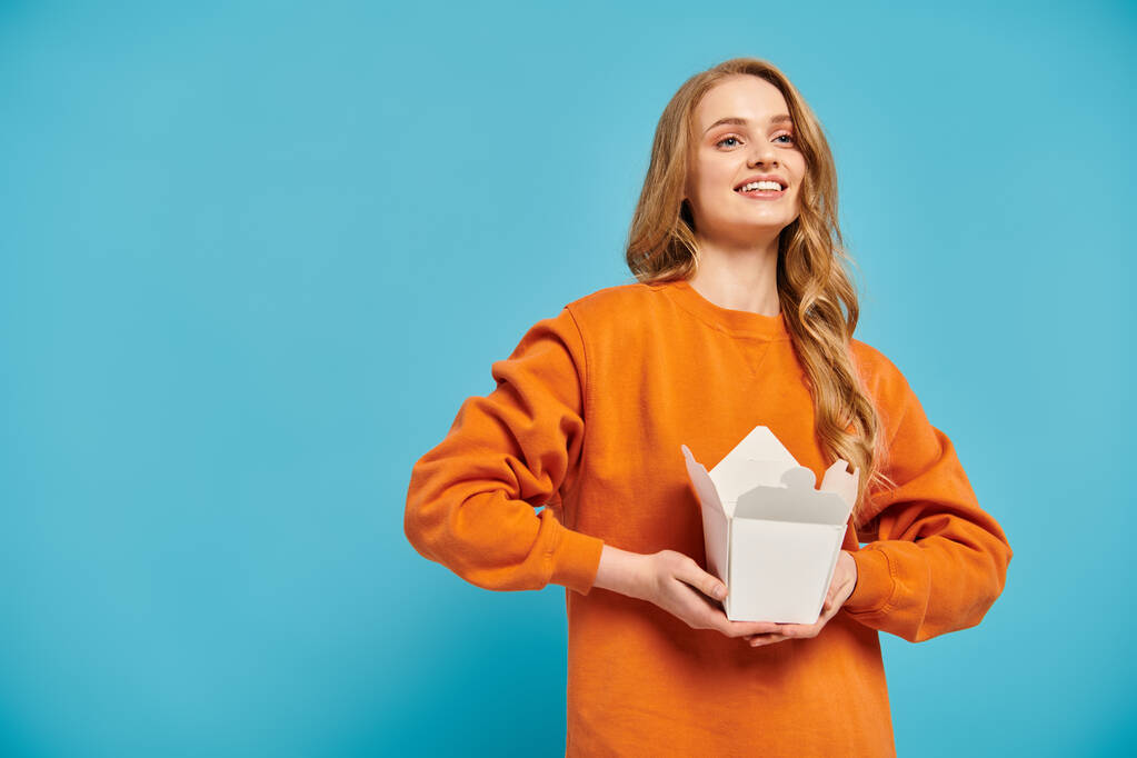 A lovely woman in an orange sweater elegantly holds a box of delicious Asian food. - Photo, Image