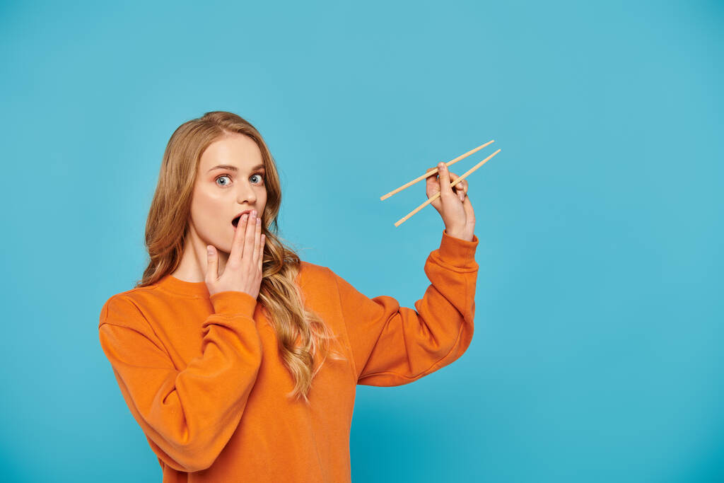 A stylish woman in an orange sweater gracefully holds a pair of chopsticks, ready to enjoy Asian cuisine. - Photo, Image