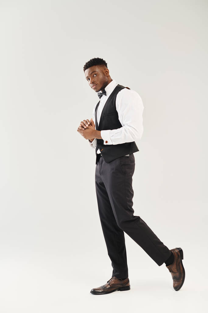 Ein junger, gutaussehender afroamerikanischer Bräutigam in Anzug, Weste und Krawatte posiert in einem Studio vor grauem Hintergrund. - Foto, Bild