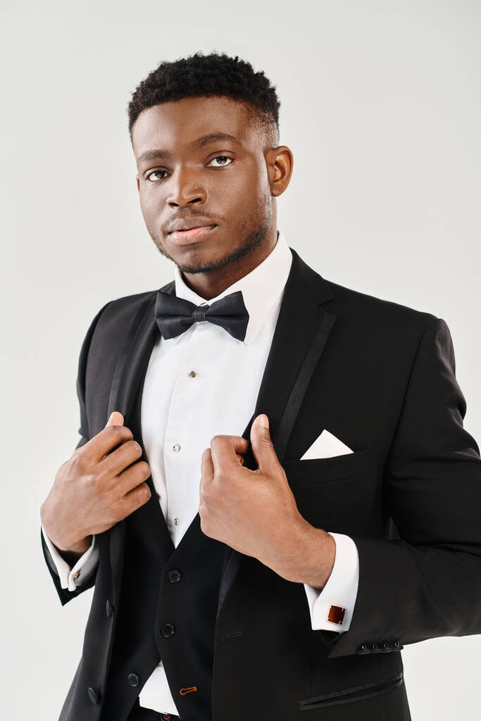 A young and handsome African American groom in a tuxedo striking a confident pose in a studio setting against a grey background. - Photo, Image