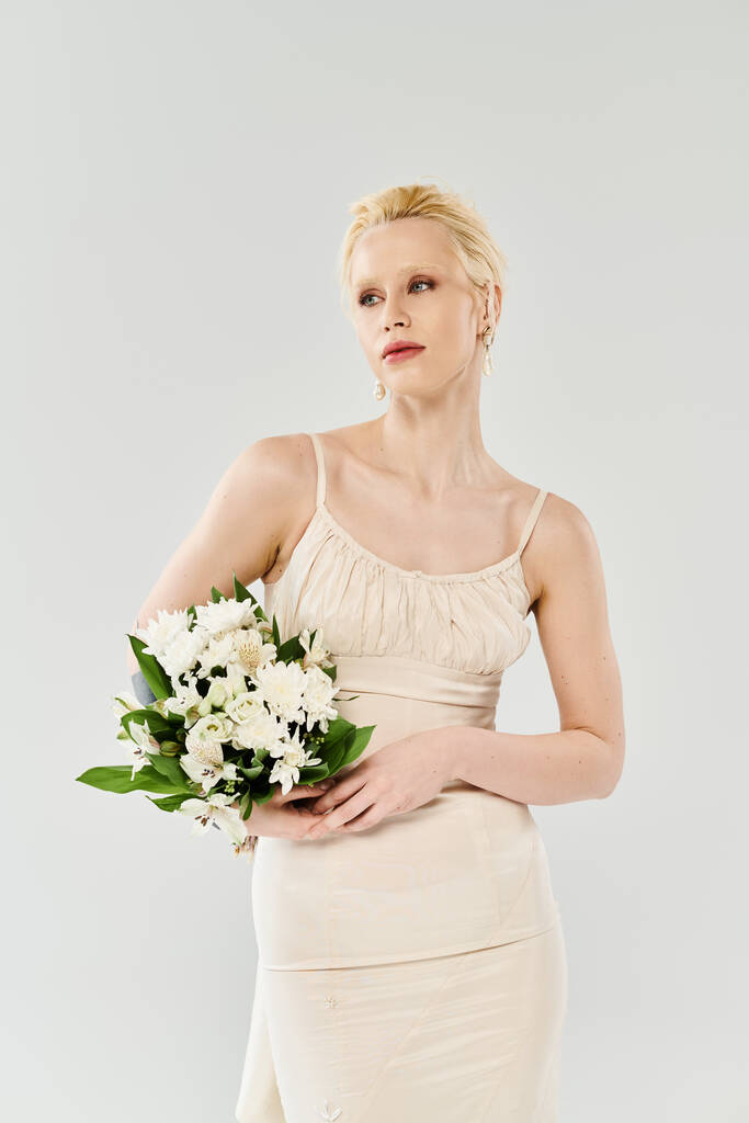 Uma noiva loira bonita em um vestido segura um buquê de flores em um estúdio contra um fundo cinza. - Foto, Imagem