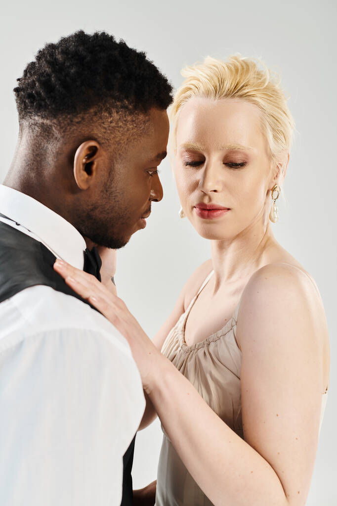 Uma noiva loira bonita em um vestido de noiva ao lado de um noivo afro-americano em um estúdio em um fundo cinza. - Foto, Imagem