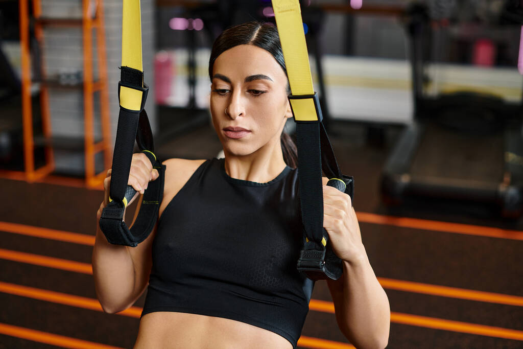 séduisante femme sportive avec des cheveux bruns dans des vêtements de sport confortables en utilisant des équipements pull-ups dans la salle de gym - Photo, image