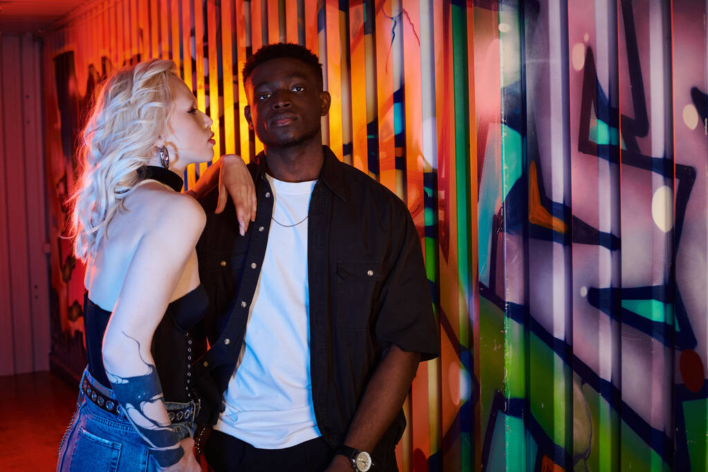 Une femme blonde et un Afro-Américain debout devant un mur urbain coloré orné de graffitis. - Photo, image