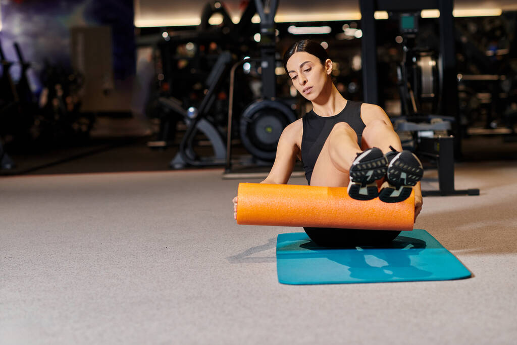 attraente donna energica in abbigliamento sportivo nero praticare su tappetino fitness con rullo mentre in palestra - Foto, immagini