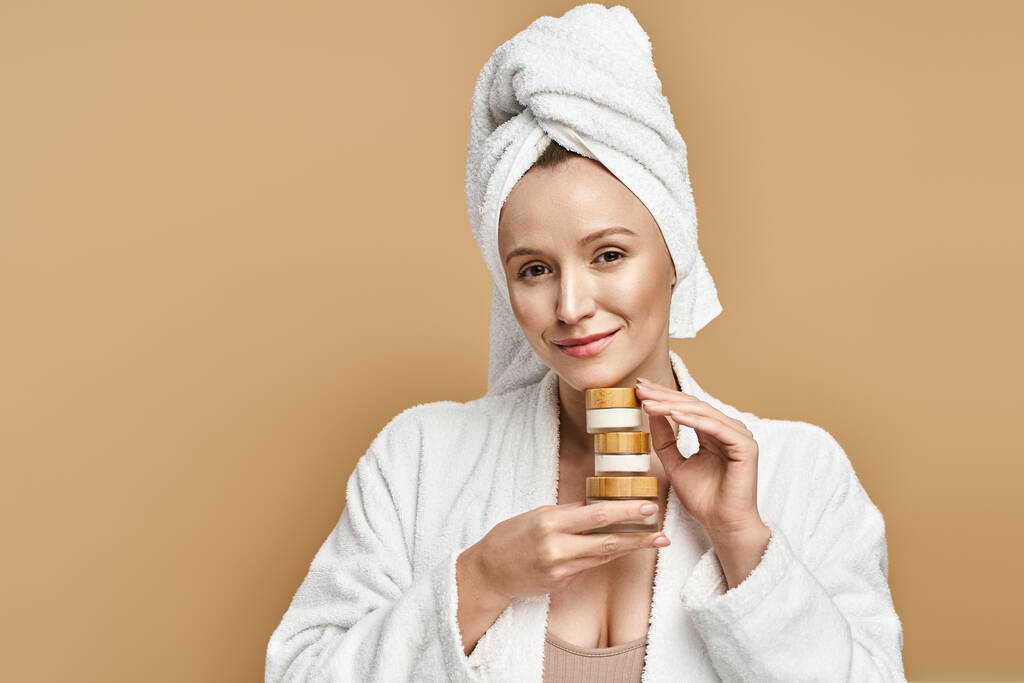 Una donna con un asciugamano in testa regge con grazia la crema, trasudando bellezza naturale e relax. - Foto, immagini
