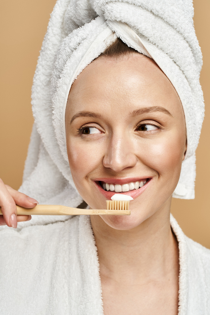 Egy természetes szépség nő aktívan mossa fogát, miközben törülközőt visel a fején.. - Fotó, kép