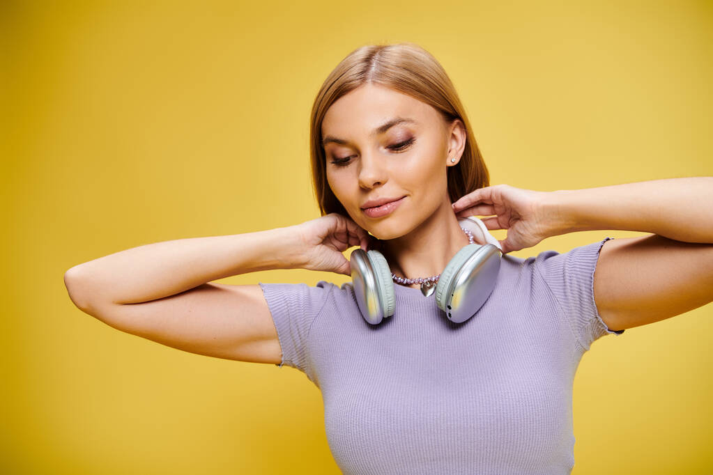 mujer alegre emocionada con el pelo corto y rubio y auriculares disfrutando de la música en el fondo amarillo - Foto, imagen