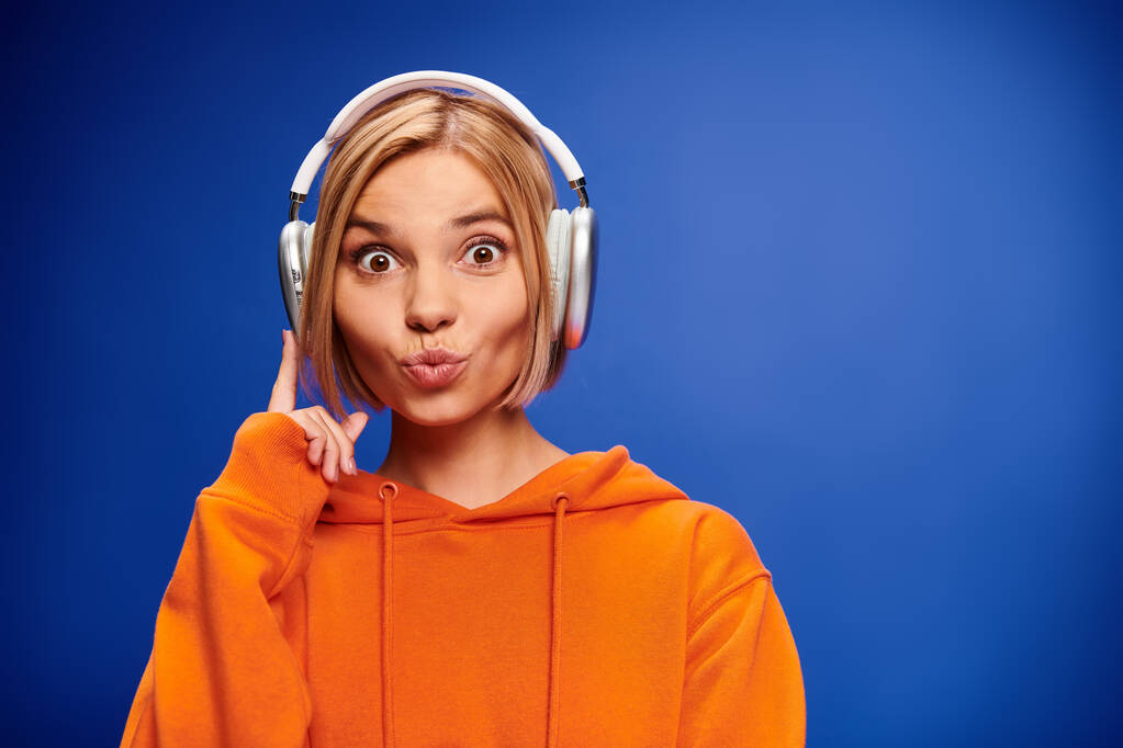 atraktivní stylová žena s krátkými blond vlasy a sluchátka těší hudbu na modrém pozadí - Fotografie, Obrázek