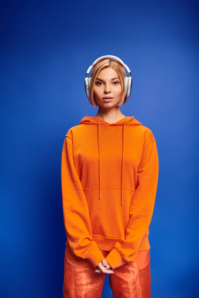 beautiful stylish woman with short blonde hair and headphones enjoying music on blue backdrop - Photo, Image