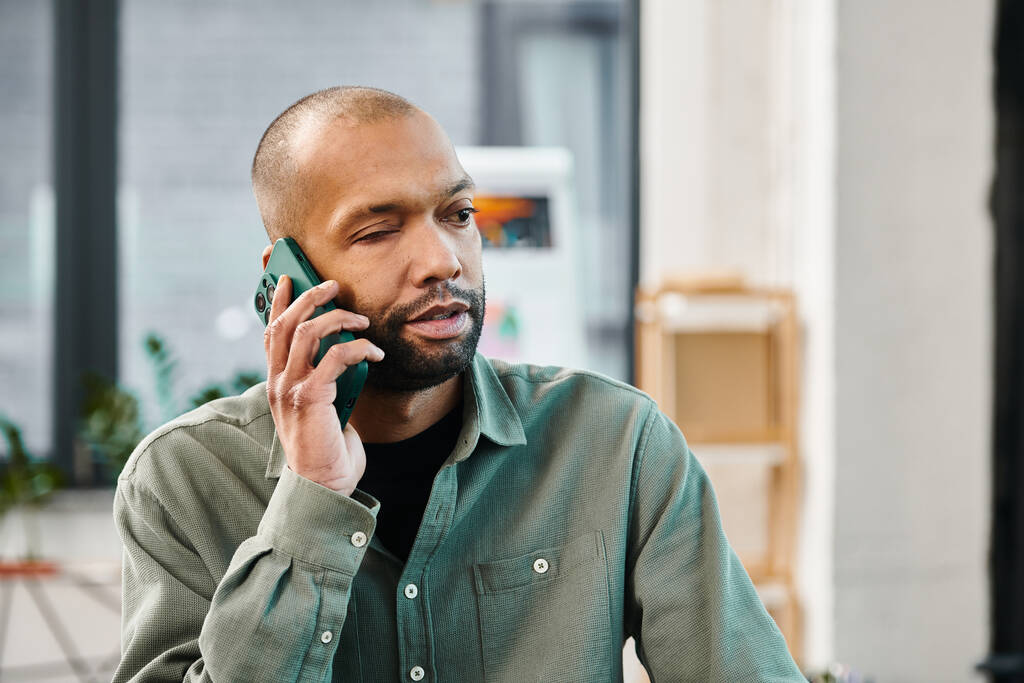 Un hombre discapacitado con miastenia grave en una camisa verde se involucra en una llamada telefónica en un entorno corporativo. - Foto, Imagen