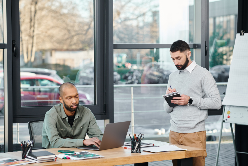 Két férfi mélységesen el van foglalva a laptopjaival, részt vesznek egy kollaboratív kódolásban egy modern irodaasztalnál, sokszínűségben és befogadásban - Fotó, kép