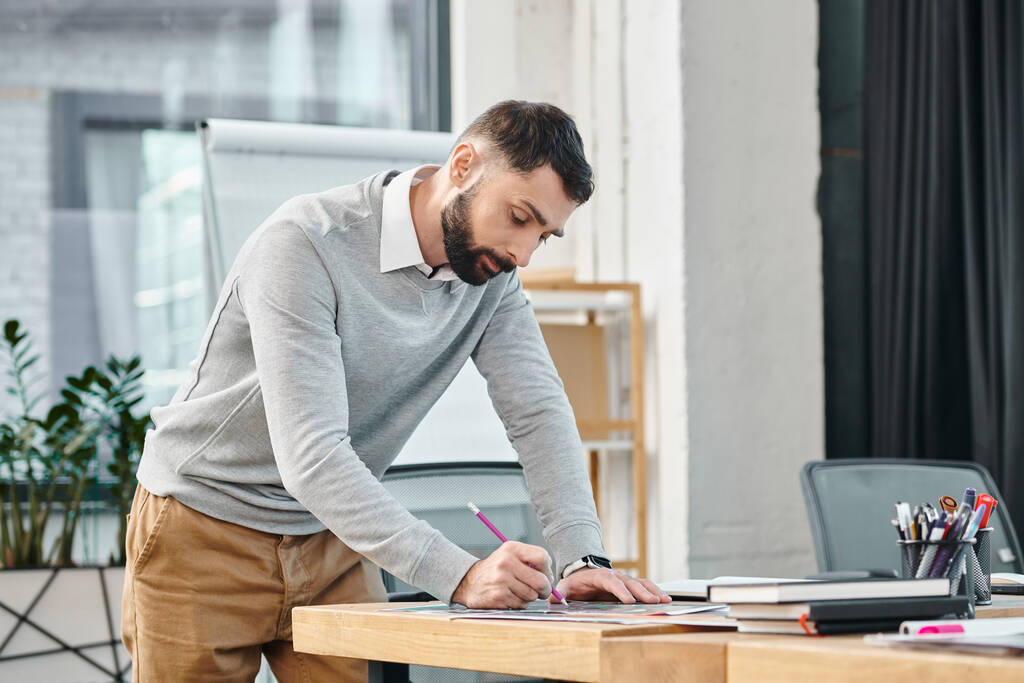 Человек, стоящий за столом, сосредоточенный, пишущий на клочке бумаги с решимостью, когда он работает над проектом в корпоративном офисе. - Фото, изображение