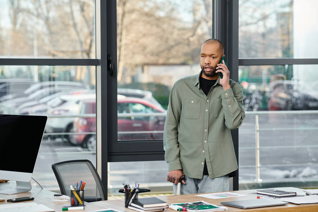 Egy myasthenia gravis-os férfi üzleti ruhában mobilon beszél, miközben egy asztal előtt áll egy irodában.. - Fotó, kép