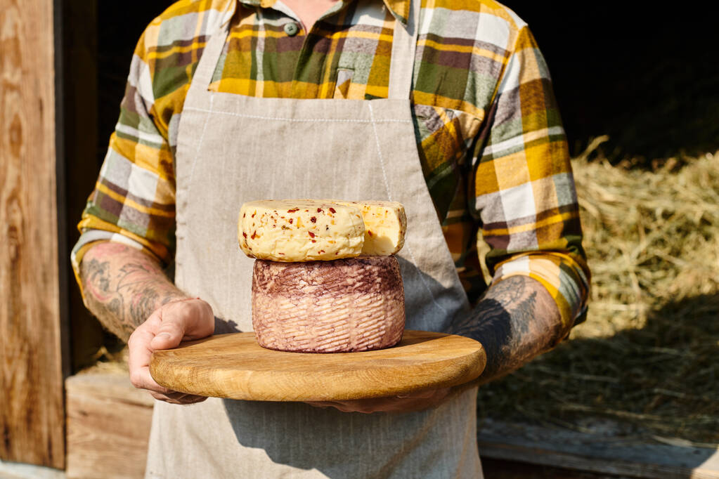 Ausgeschnittene Ansicht eines erwachsenen Bauern mit Tätowierungen in Freizeitkleidung, der selbst gemachten Käse in den Händen hält - Foto, Bild