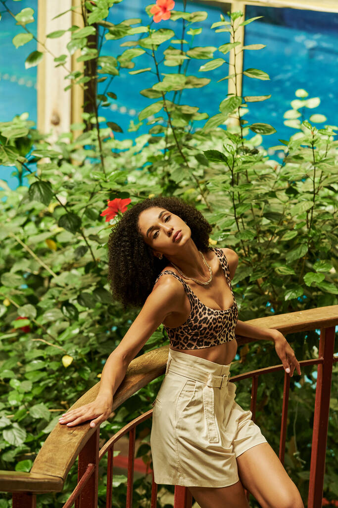молода афроамериканка з кучерявим волоссям позує на металевому мосту в зеленому саду - Фото, зображення