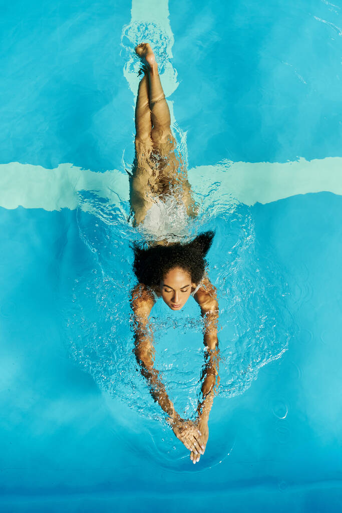 top view of young african american woman swimming in clear pool water, serene and peaceful - Photo, Image