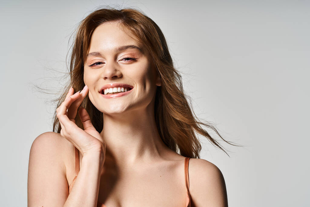 Schönheitsporträt einer lächelnden Frau mit trendigem Make-up, die in die Kamera auf grauem Studiohintergrund blickt - Foto, Bild