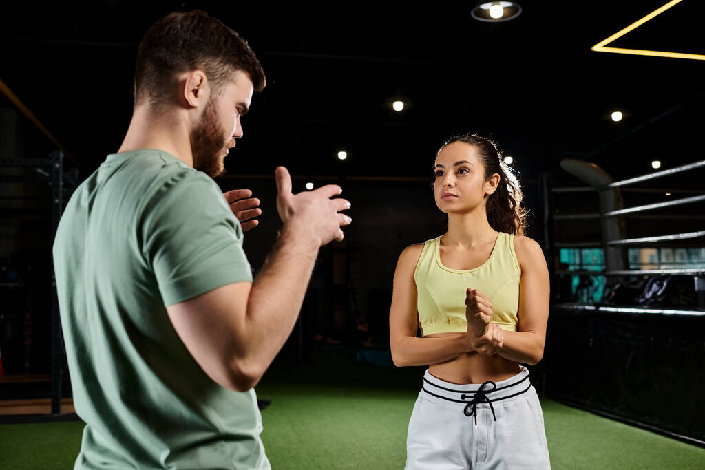 Ένας άνδρας εκπαιδευτής επιδεικνύει τεχνικές αυτοάμυνας σε μια γυναίκα σε ένα γυμναστήριο, εστιάζοντας στην ενδυνάμωση και την οικοδόμηση δεξιοτήτων. - Φωτογραφία, εικόνα