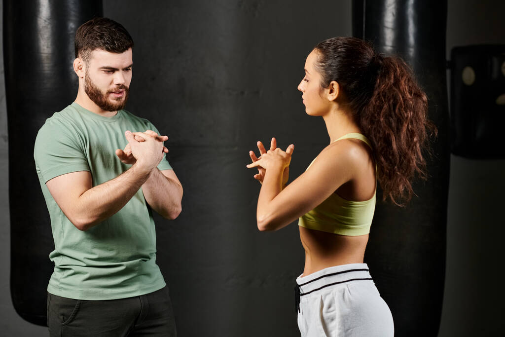 Egy férfi edző vezet egy nőt önvédelmi tréningen, együtt állnak egy boxzsák előtt a tornateremben.. - Fotó, kép