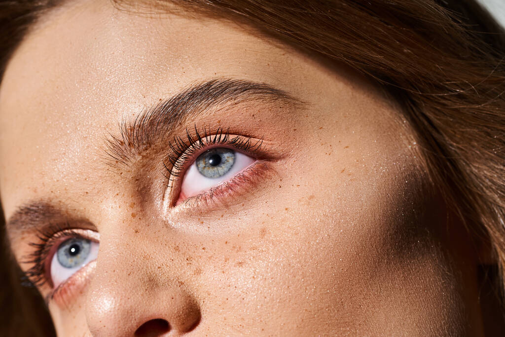 Κοντινό πορτρέτο ομορφιάς της γυναίκας μπλε μάτια με ροδακινί μακιγιάζ και φακίδες σε γκρι φόντο - Φωτογραφία, εικόνα