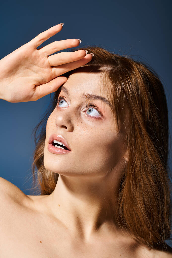Zvědavá žena s broskvovým make-upem a pihami, dotýká se čela a dívá se na modré pozadí - Fotografie, Obrázek