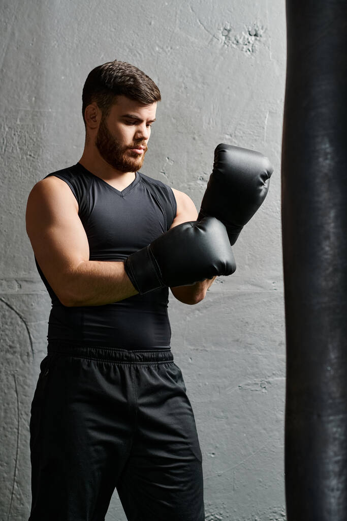 Красивый мужчина с бородой стоит рядом с боксерской грушей в тренажерном зале, практикуя технику бокса с сосредоточенностью и решимостью. - Фото, изображение