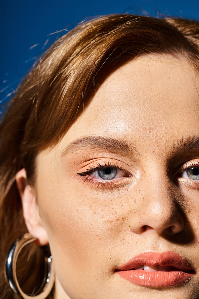 Nahaufnahme Schönheit Porträt einer Frau Gesicht mit blauen Augen, Pfirsich Make-up und Sommersprossen auf blauem Hintergrund - Foto, Bild