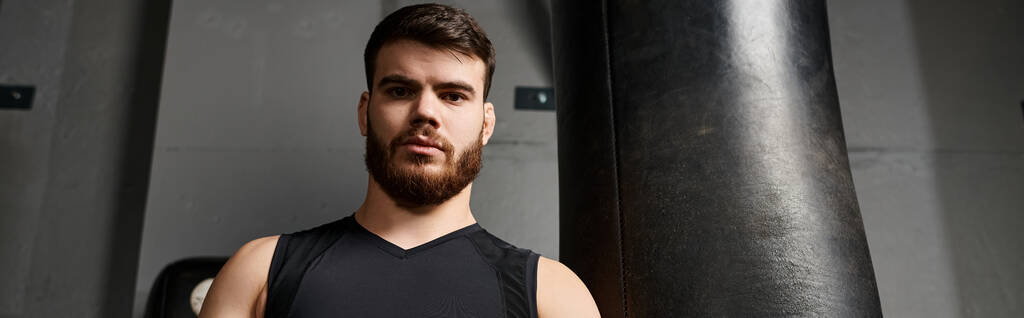 Un bel homme avec une barbe boxe à côté d'un sac de boxe dans une salle de gym. - Photo, image