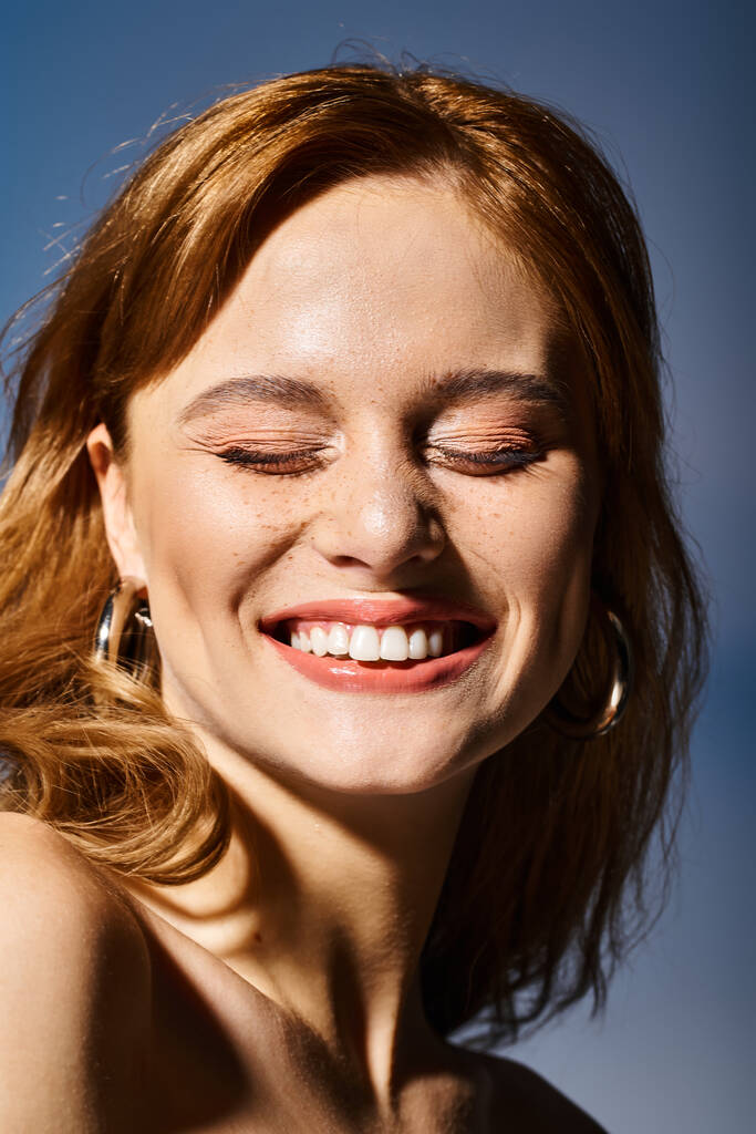 Κοντινό πλάνο μιας πολύ ελκυστικής γυναίκας που χαμογελάει με κλειστά μάτια, σε μπλε φόντο - Φωτογραφία, εικόνα